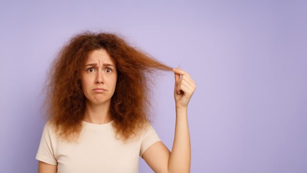 Vrouw met pluizig, ontregeld haar kijkt bezorgd terwijl ze een pluk haar vasthoudt tegen een lavendel achtergrond.