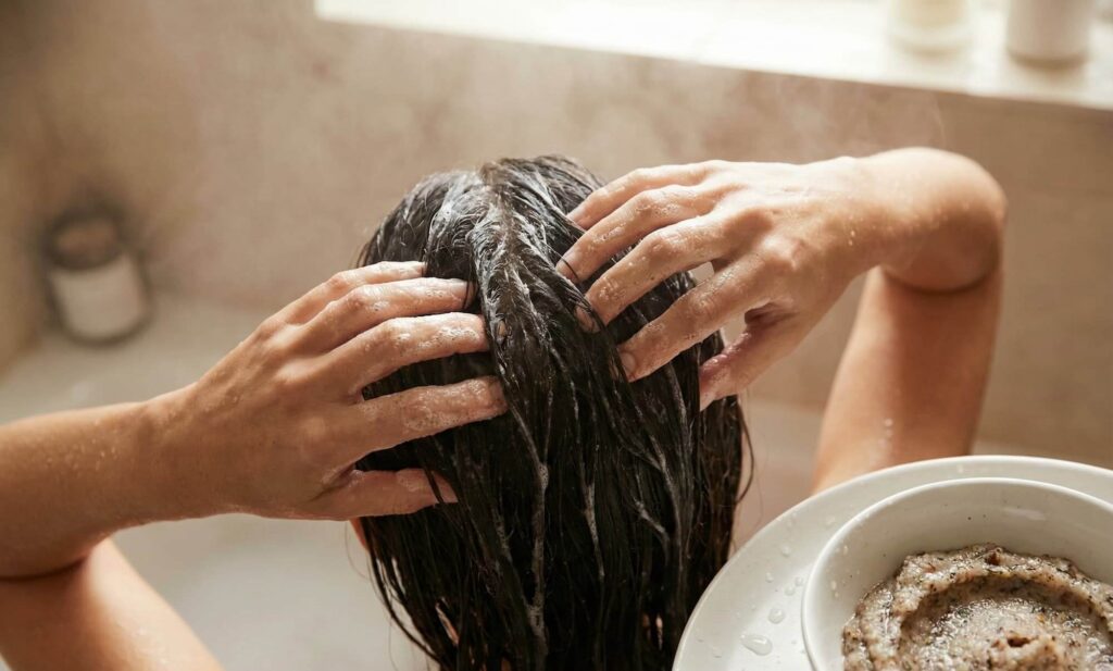 Vrouw masseert haar hoofdhuid met een scalp scrub in de badkamer