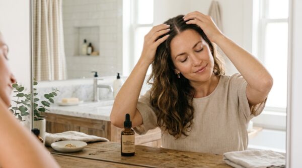 Een vrouw die rustig haarserum aanbrengt op haar hoofdhuid met haar vingertoppen in een lichte badkamer.